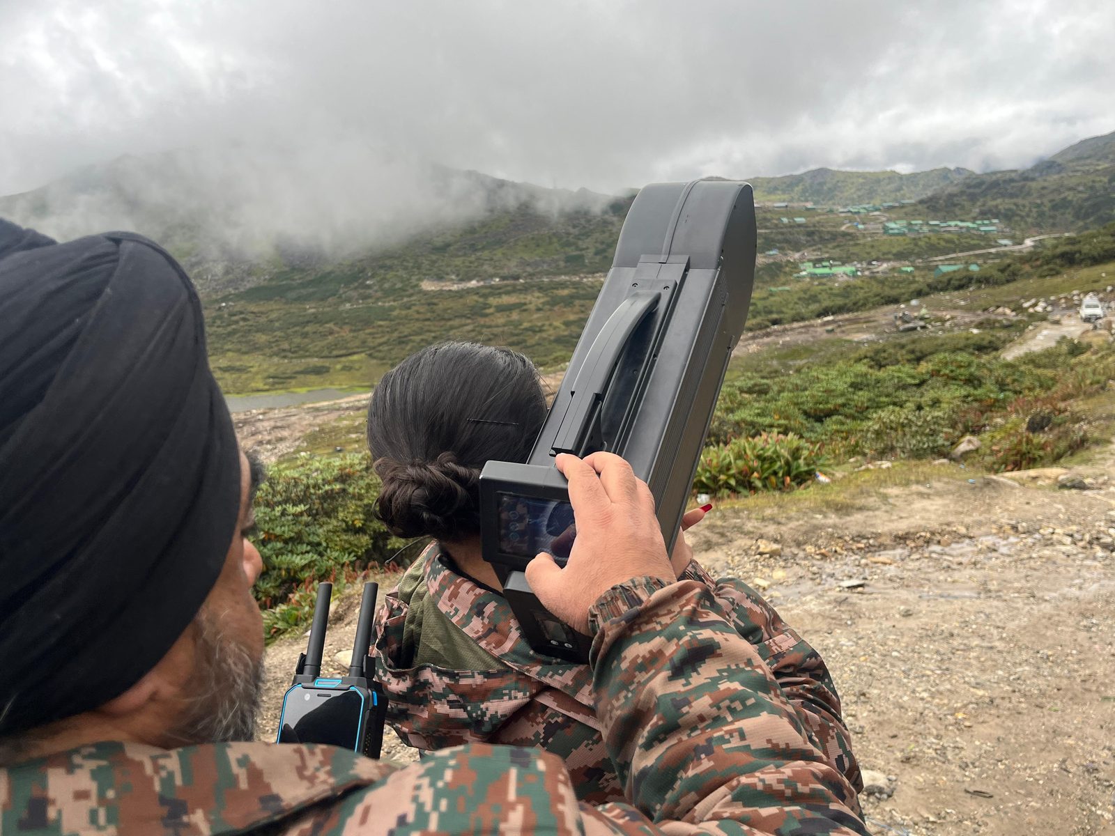 Soldiers operating a handheld anti-drone jammer with display screen on misty mountain terrain