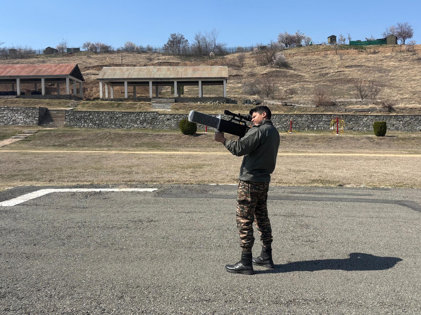 Soldier aiming a rifle-style anti-drone jammer with precision scope in an open field trial